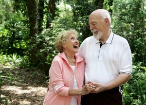 A happy, active senior couple laughing together on a walk through the park. She's wearing a hearing aid. 